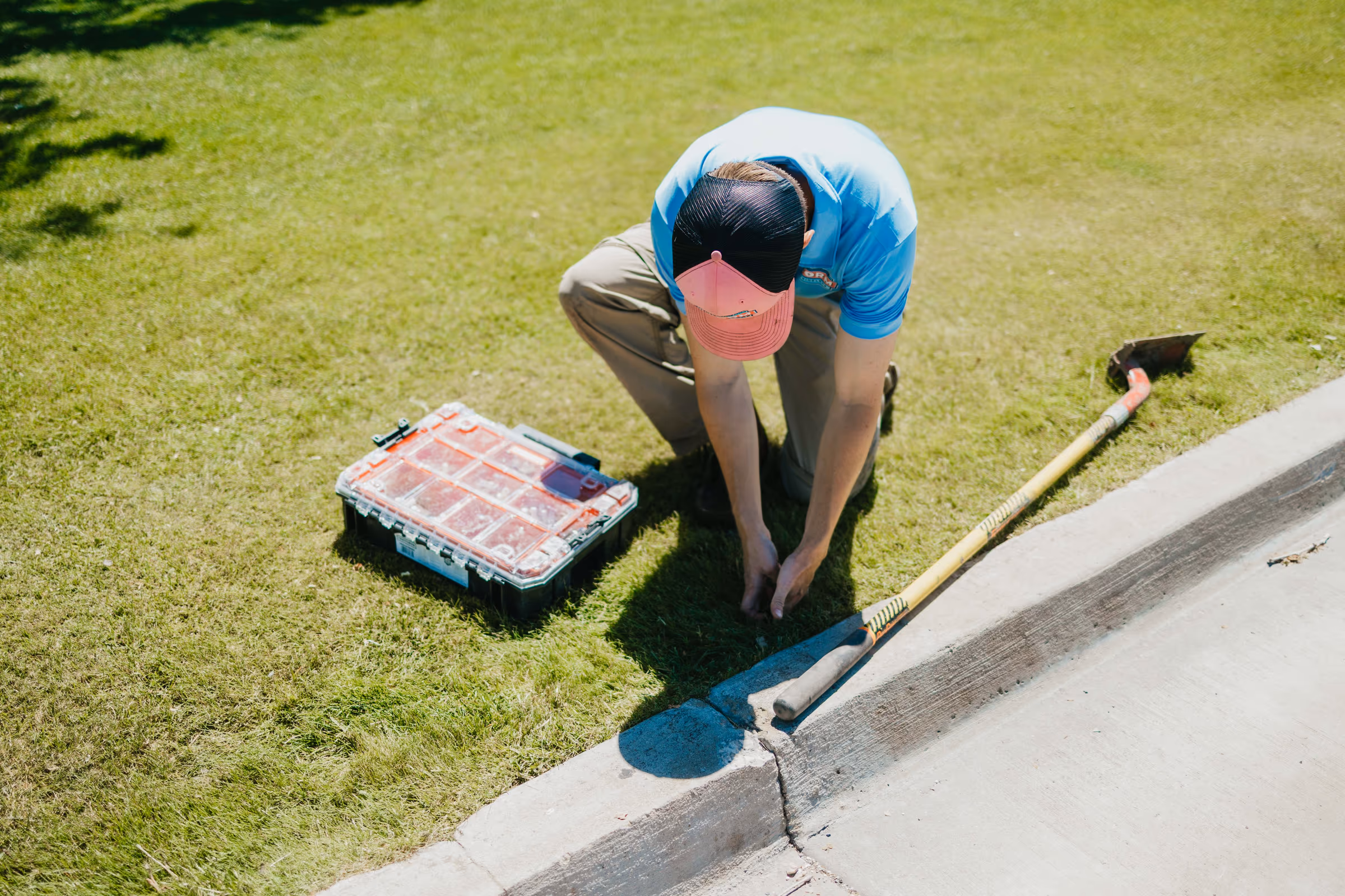 Storm Sprinklers technician kneeling by a curb repairing a lawn sprinkler with tools nearby